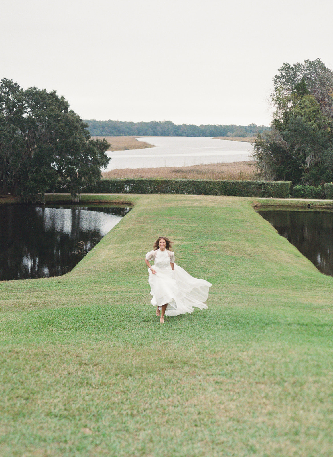 Bride in white dress running through field at Middleton Place in Charleston, SC
